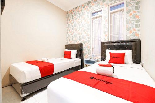 two beds in a room with red and white at RedDoorz Syariah Near Jam Gadang Bukit tinggi 2 in Bukittinggi