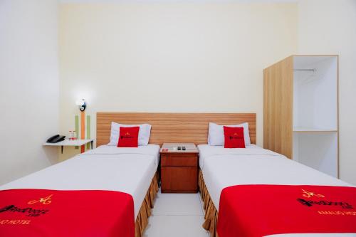 two beds in a small room with red sheets at RedDoorz Plus at Amalio Hotel Surapati in Bandung