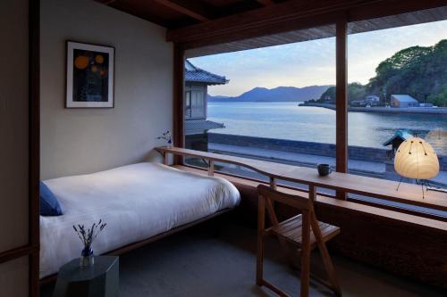 ein Schlafzimmer mit großem Fenster, ausgestattet mit einem Bett und einem Schreibtisch in der Unterkunft SOIL Setoda in Onomichi