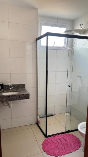 a bathroom with a glass shower and a pink rug at Brisas do Lago 2 Quartos in Palmas