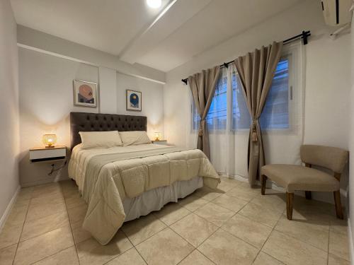 a bedroom with a bed and a chair and a window at Campana Suites Becerra in Campana