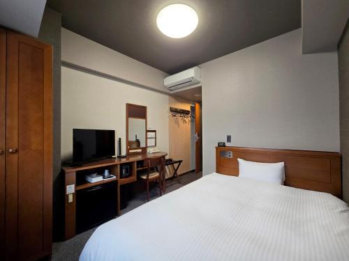 a bedroom with a bed and a desk with a television at Hotel Route-Inn Shimodate in Chikusei