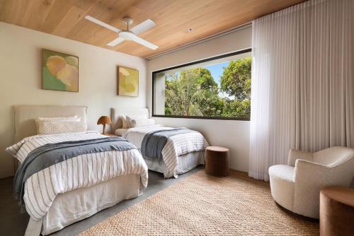 two beds in a bedroom with a window and a chair at Villa Alcorn in Suffolk Park