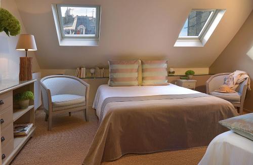 a bedroom with a bed with two chairs and two windows at Hôtel Le Fer à Cheval in Trouville-sur-Mer