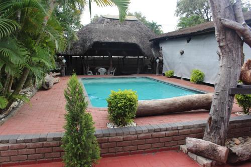 a house with a swimming pool with a thatch roof at Charming Self Catering Apartment in Phalaborwa