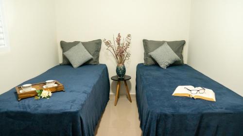 two beds in a room with blue sheets and a vase at Jahu Center Casas Un 6 in Jaú