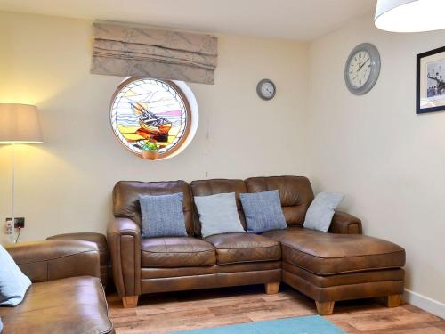 a living room with a brown leather couch and a clock at Porthole Cottage in Allonby