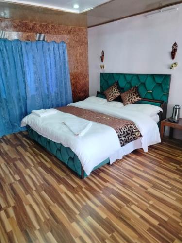 two beds in a bedroom with blue curtains and wooden floors at Siachen Hotel in Kargil