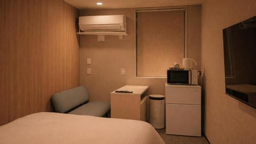 a small room with a bed and a chair and a microwave at ホテルクレイドルキャビン田無 in Nishitokyo