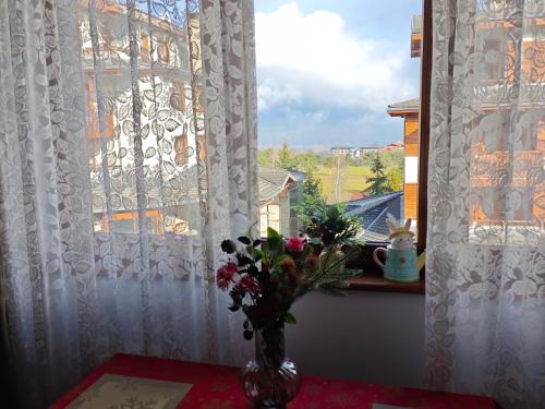a vase with flowers on a table in front of a window at Bansko Pirin Golf & Country Club Blue Mountains View in Razlog