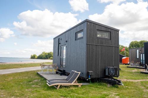a black tiny house with a chair and a table at Tiny SeaSide - Loddenhøj in Lillekobbel