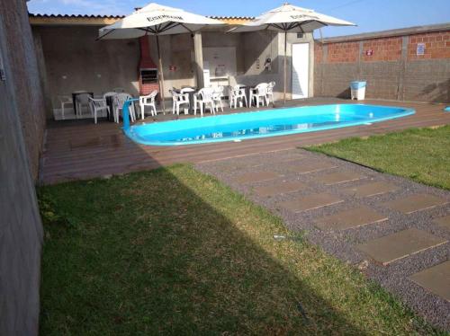 a backyard with a swimming pool with chairs and an umbrella at QUARTO CONTEINER, EDICULA ABERTA E PISCINA AQUAVibes in Cascavel