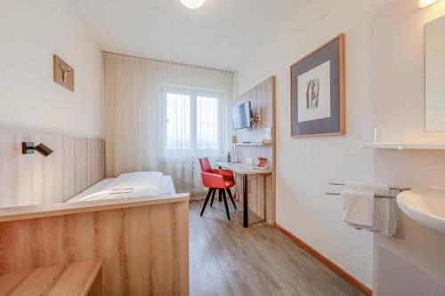 a bathroom with a sink and a desk with a red chair at Hotel St Elisabeth in Allensbach