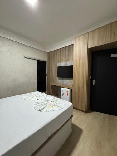 a bedroom with a large white bed with a flat screen tv at Hotel Samaritano in Montes Claros