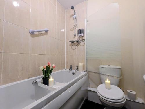 a bathroom with a tub and a toilet and candles at Sherlock's Moray House -Idea long stay for contractors & family Two bedroom mid terrace 3 beds 2 sofa beds Sleep 5 Working facility Free WiFi TV & private parking Enclose rear garden dog friendly Sainsbury's & takeaway pubs in walking distance in Church Gresley