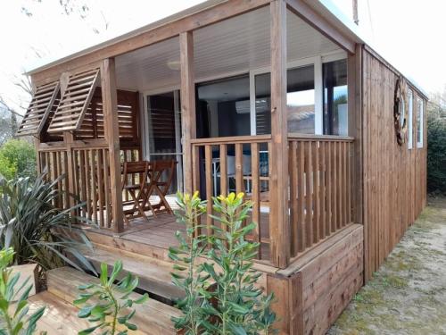 a wooden house with a deck with a chair at ZEcamping 3 étoiles avec piscine chauffée - bar et restaurant in Pézenas
