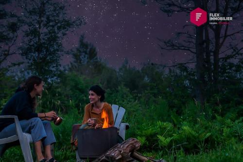 two people sitting in chairs under a starry sky at Le Pèlerin - Chalet rustique Écoresponsable en nature - Estrie in Notre-Dame-Des-Bois