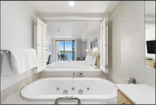 a white bathroom with a tub and a bedroom at Water Front Retreat Ballina in Ballina