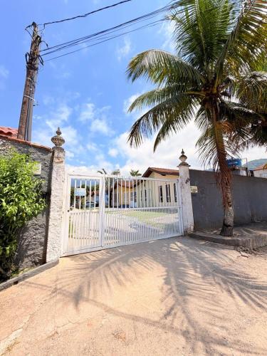 a white gate with a palm tree in front of a house at Casa em Condomínio com Wi-Fi - 300m da praia in Ubatuba
