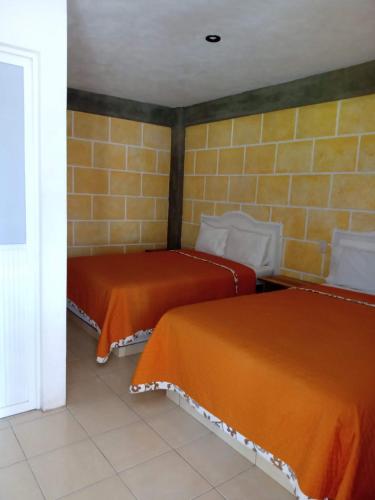 two beds with orange sheets in a room at Hotel de la Cruz in Maguey Blanco