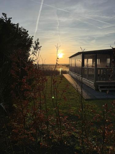 a house with the sun setting in a field at Het mooiste plekje van het park in Kropswolde