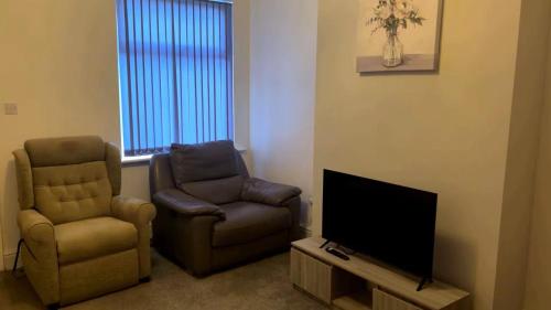 a living room with two chairs and a flat screen tv at PLUS Properties Moston in Stoke on Trent