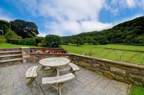 a wooden table and benches on a patio with a stone wall at 3 Bed in Fishguard oc-wav276 in Pontfaen
