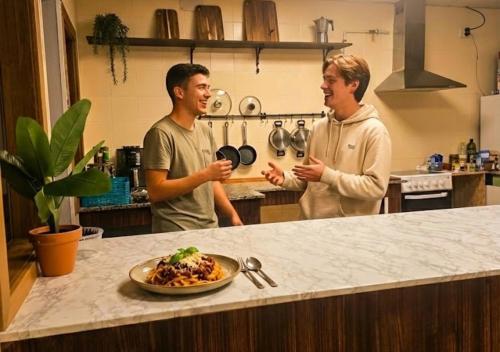 two men standing in a kitchen with a plate of food at Hostel Cangas Backpackers in Cangas de Morrazo
