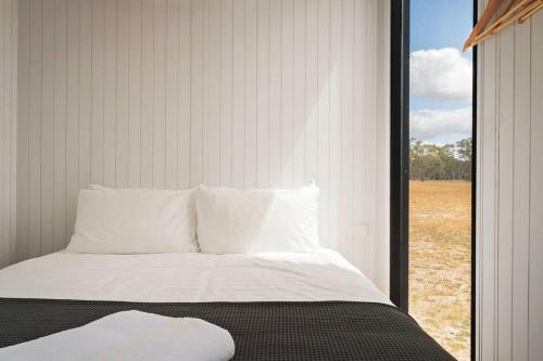 a bed with white pillows and a large window at Bellellen Park 1 by Tiny Away in Stawell