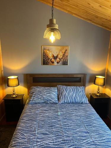 a bedroom with a bed with a blue comforter and two lamps at cabaña alerce lago panguipulli in Panguipulli