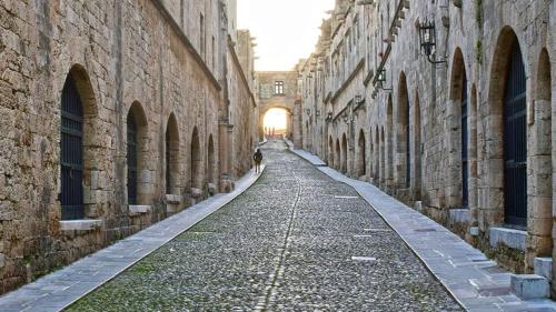 an empty alley between two stone buildings with the sun in the distance at Periklis House in Ixia