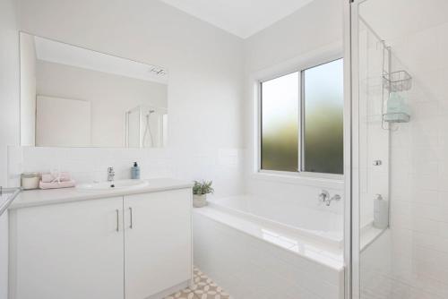 a white bathroom with a tub and a sink at Beach by the Dunes in Goolwa South