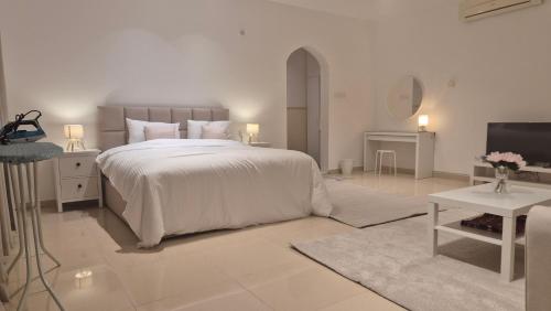 a white bedroom with a large bed and a television at بيت الشّاب Al Shab House in Ţīwī