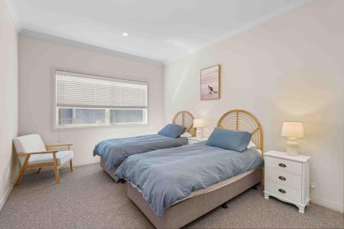 a bedroom with two beds and a chair and a window at Aerial Blue Mollymook in Mollymook