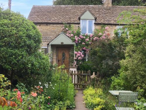 an old stone house with a wooden door and flowers at Folly Cottage in Avening