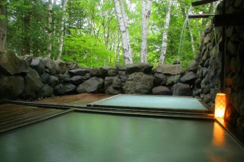 a pool of water with a stone wall and trees at Shibu Tatunokan in Chino