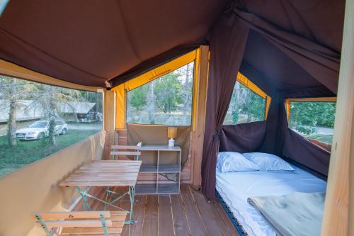 a tent with a bed and a table in it at Camping Onlycamp du lac de Roybon in Roybon
