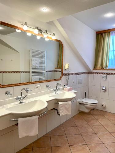 a bathroom with two sinks and a toilet and a mirror at Gasthof & Hotel Jägerwirt in Aufhofen