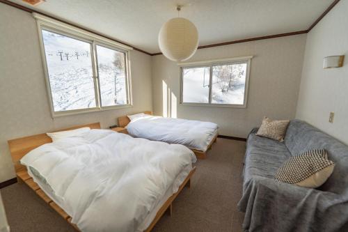 a bedroom with two beds and a couch and two windows at 北国ロッヂ in Otari