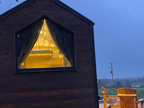 a large window in a wooden shed with a chair at Badgers Hollow by Tiny Away in Whitchurch