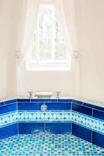 a bathroom with a blue tiled tub with a window at Ile Des Deux Cocos in Blue Bay