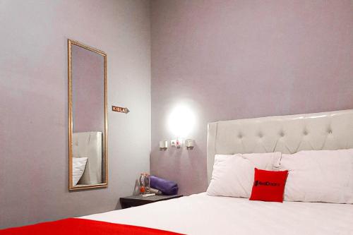 a bedroom with a bed with a red pillow and a mirror at RedDoorz at Deluxe Hotel near Terminal Purabaya Bungurasih in Sidoarjo