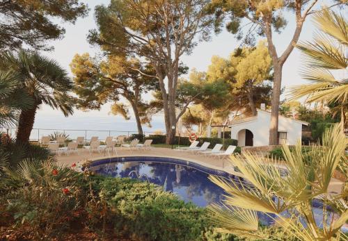 ein Pool mit Stühlen und Bäumen und dem Meer in der Unterkunft Hotel Bendinat in Portals Nous