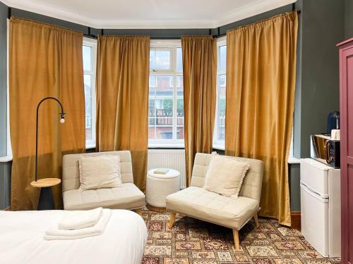 a bedroom with two chairs and a bed and windows at Zozy Anson in London