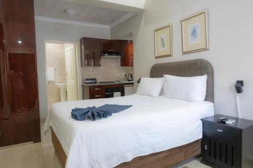 a bedroom with a large white bed and a kitchen at Innisfree Apartments in Gaborone