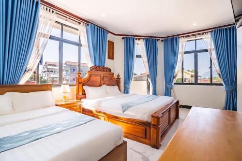 a bedroom with two beds and blue curtains and windows at Boeung Prolet Guest House in Kampot