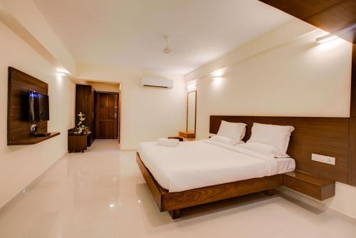 a bedroom with a bed with white sheets and a television at Hotel BMS in Mangalore