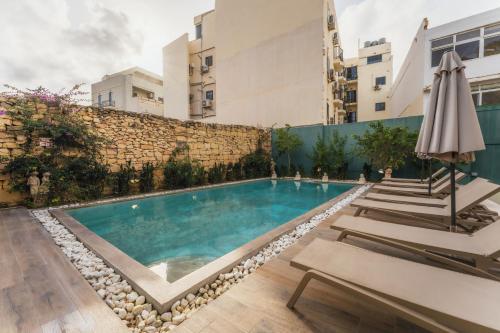 a swimming pool with lounge chairs and an umbrella at Suite 2 at Palazzo Seraphim Boutique living in St Julians in St. Julianʼs
