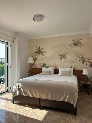 a bedroom with a large bed with palm trees on the wall at Charm-In Apartments in Vila Nova de Milfontes