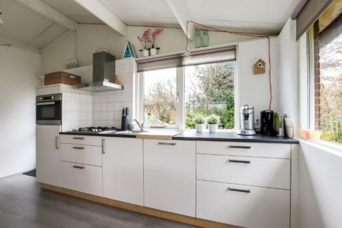 a kitchen with white cabinets and a large window at Rekerlanden 195 in Schoorldam